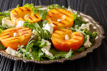 Delicious appetizer salad of grilled fresh peaches, with feta cheese, arugula, peanuts and herbs close-up on a plate. horizontal
