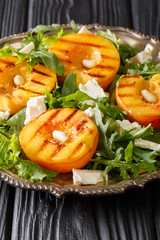 Dietary vegetarian salad with grilled peaches, with feta cheese, arugula, peanuts and herbs close-up on a plate on a table. vertical