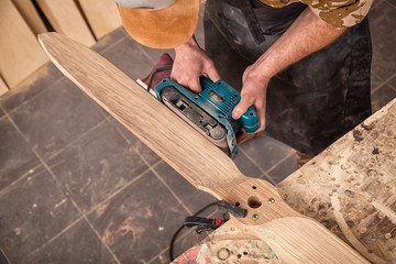 Close up of an young man builder carpenter equals polishes wooden board with a  random orbit sander...