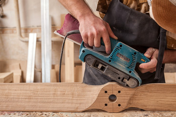 Close up of an young man builder carpenter equals polishes wooden board with a  random orbit sander  in the workshop