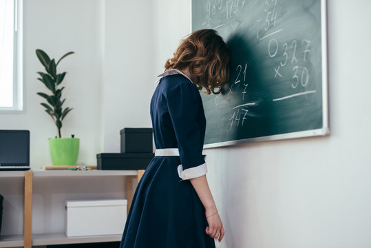 Sad schoolgirl standing in front of blackboard.