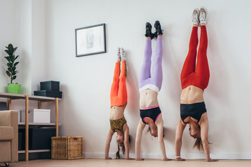 Females doing handstand pose near wall. Mother and daughters exercising at home, sport, family