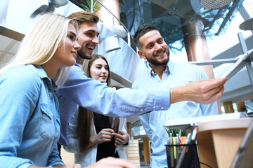 Obraz premium Group of young people in casual wear sitting at the office desk and discussing something while looking at PC together.