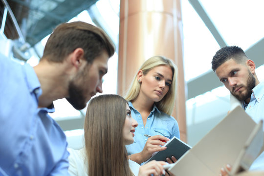 Group of young people in casual wear sitting at the office desk and discussing something while looking at PC together.