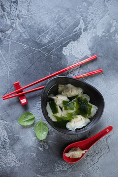 Bowl of wonton soup on a grey concrete background, view from above with copyspace, vertical shot