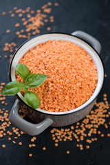 Dried split raw red lentils in a pot, elevated view on a black stone background, vertical shot