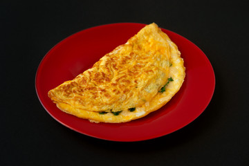 French omelette on a red saucer and black background. Omelet from eggs, grated cheese and parsley for a healthy breakfast. Omelette on a black background looks strictly and concisely.