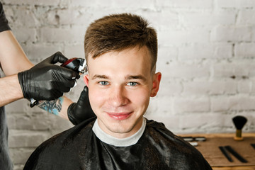 Barber does hair cut young guy on a brick wall background.
