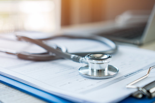 Stethoscope on prescription clipboard record on hospital office with Laptop computer at doctor work office in hospital or clinic with light flare, Concept of Health Care and Medical. Selective focus.