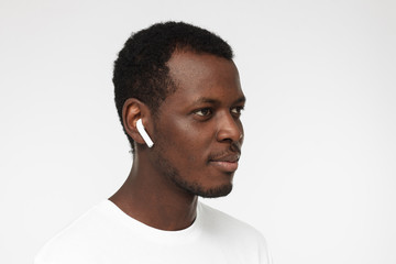 Close up headshot of young smiling african american man wearing blank white t shirt, listeting to his favorite music track