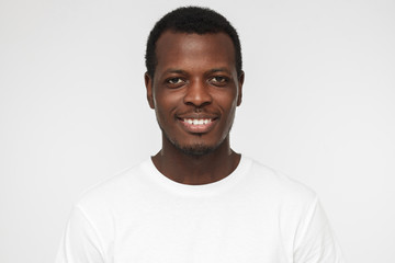 Close up shot of smiling attractive african american man in blank white t-shirt isolated on gray background