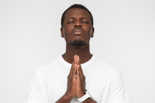Young african american man isolated on gray background looking stressed, putting hands together as if he is praying with closed eyes to overcome depression