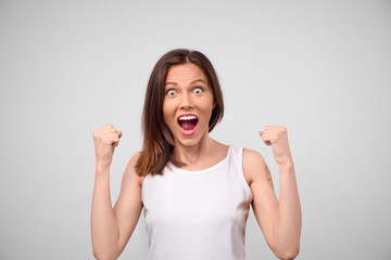 Stun beautiful woman in casual clothes celebrating her victory raising hands clenching fists having happiness and satisfaction. Female rejoicing her entering to university. Reaching goals and aims