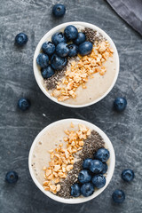 Smoothie bowls with banana, chia seeds, fresh blueberry and nuts over grey table.