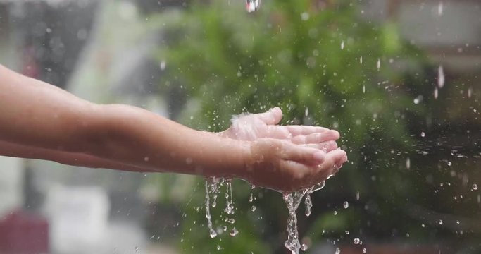 Close-up of a child putting his hand in the rain, and you see the drops bouncing on his hand. Concept of: nature, water, global warming