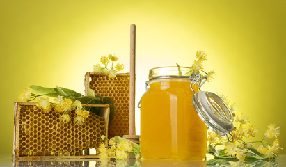 Wooden frames with wax honeycomb and honey in jar, on yellow background