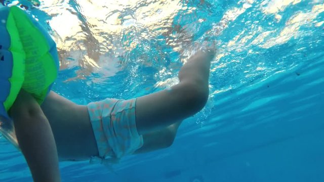 Little boy learning to swim in a swimming pool. Shoot from underwater