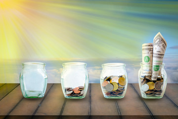 The coins in bottle on green and sky background. The ray sun on  the coins in the bottle on old wood. The concept of growth for the save money.