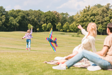 parents looking at daughter playing with colorful kite in park