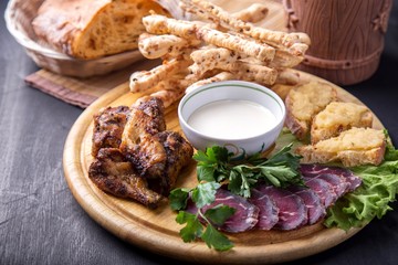 Tasty beer snack with chicken wings, pastrami and breadsticks with sauce