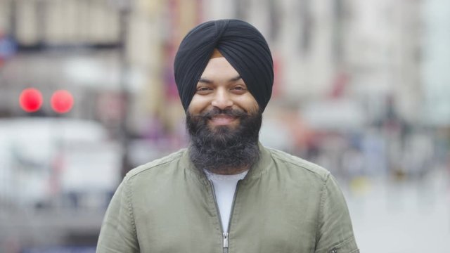 Portrait of young Indian male wearing a turban and smiling to camera, in slow motion
