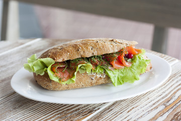 Аппетитный бутерброд с лососем и салатом на белой тарелке