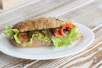 Аппетитный бутерброд с лососем и салатом на белой тарелке
