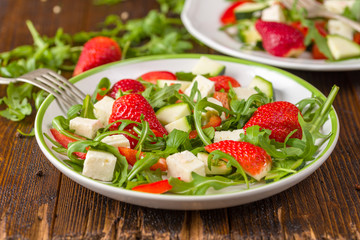 Fresh vegetable strawberry salad on white plate on natural rustic desk.