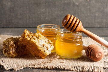 Honey dripping from a wooden honey dipper in a jar on wooden grey rustic background