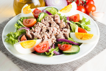 Fresh fish tuna salad made of tomato, ruccola, tuna, eggs, arugula, crackers and spices. Caesar salad in a white bowl on wooden background