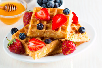 Photo of fresh homemade food made of berry Belgian waffles with honey, chocolate, strawberry, blueberry, maple syrup and cream. Healthy dessert breakfast concept with juice. 