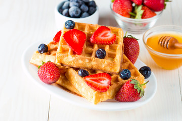 Photo of fresh homemade food made of berry Belgian waffles with honey, chocolate, strawberry, blueberry, maple syrup and cream. Healthy dessert breakfast concept with juice. 
