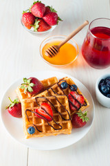 Photo of fresh homemade food made of berry Belgian waffles with honey, chocolate, strawberry, blueberry, maple syrup and cream. Healthy dessert breakfast concept with juice. 