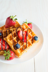 Photo of fresh homemade food made of berry Belgian waffles with honey, chocolate, strawberry, blueberry, maple syrup and cream. Healthy dessert breakfast concept with juice. 