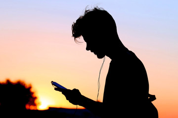 silhouette of a man with a mobile phone and headphones at sunset.