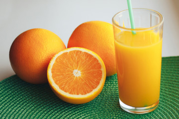 Glass with orange juice next to orange slices on a white and green background.