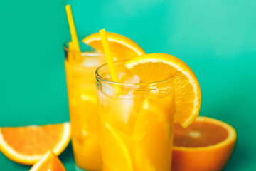 Glasses of orange juice with ice and orange slices on a green background.