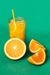Glasses of orange juice with ice and orange slices on a green background.