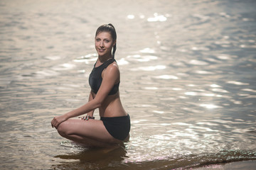 Fototapeta na wymiar young brunette in black swimsuit sitting in the water against the sea landscape