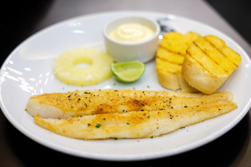 Grilled dolly fish with black pepper, mayonnaise sauce, lemon, pineapple and garlic bread recipe serve on white plate - food concept.