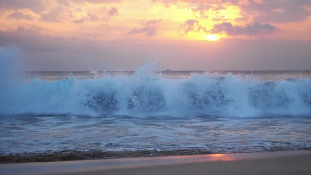 Great waves of a powerful ocean break into foam during beautiful sunset on the island of Bali on beautiful cloudy sky on the background. 3840x2160