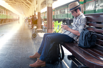 Asian man wearing a hat weave sitting playing games on mobile. While waiting for the train. At station in the outbound platform.