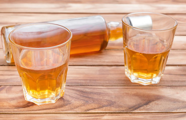 Two glasses of whisky with bottle of whiskey on wooden background.