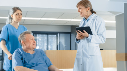 Obraz premium In the Hospital Lobby, Nurse Pushes Elderly Patient in the Wheelchair, Doctor Talks to Them while Using Tablet Computer. Clean, New Hospital with Professional Medical Personnel.