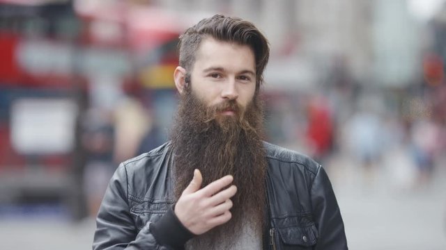 Young man with a long beard smiling to camera and stroking his beard, in slow motion