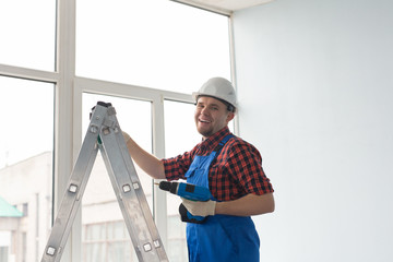 Happy male builder standing on ladder with drill infront of window.