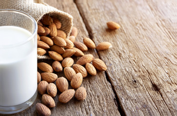 A pile of almonds and a glass of milk on the wooden table.