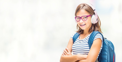Fototapeta premium Portrait of modern happy teen school girl with dental braces glasses bag backpack and headphones