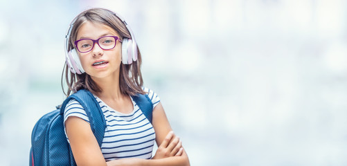Portrait of modern happy teen school girl with dental braces glasses bag backpack and headphones