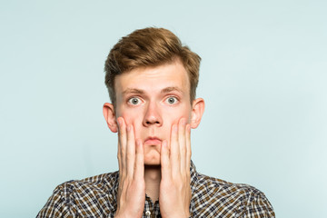 shocked speechless gobsmacked stunned man clutching his face. portrait of a young guy on light...